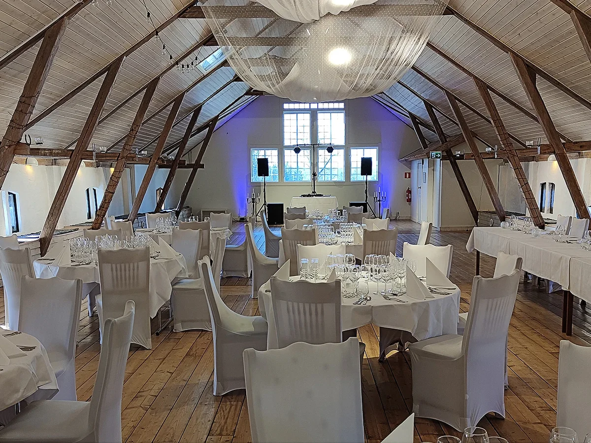 Ljus bröllopslokal i lada med dukade bord och teknik för middag