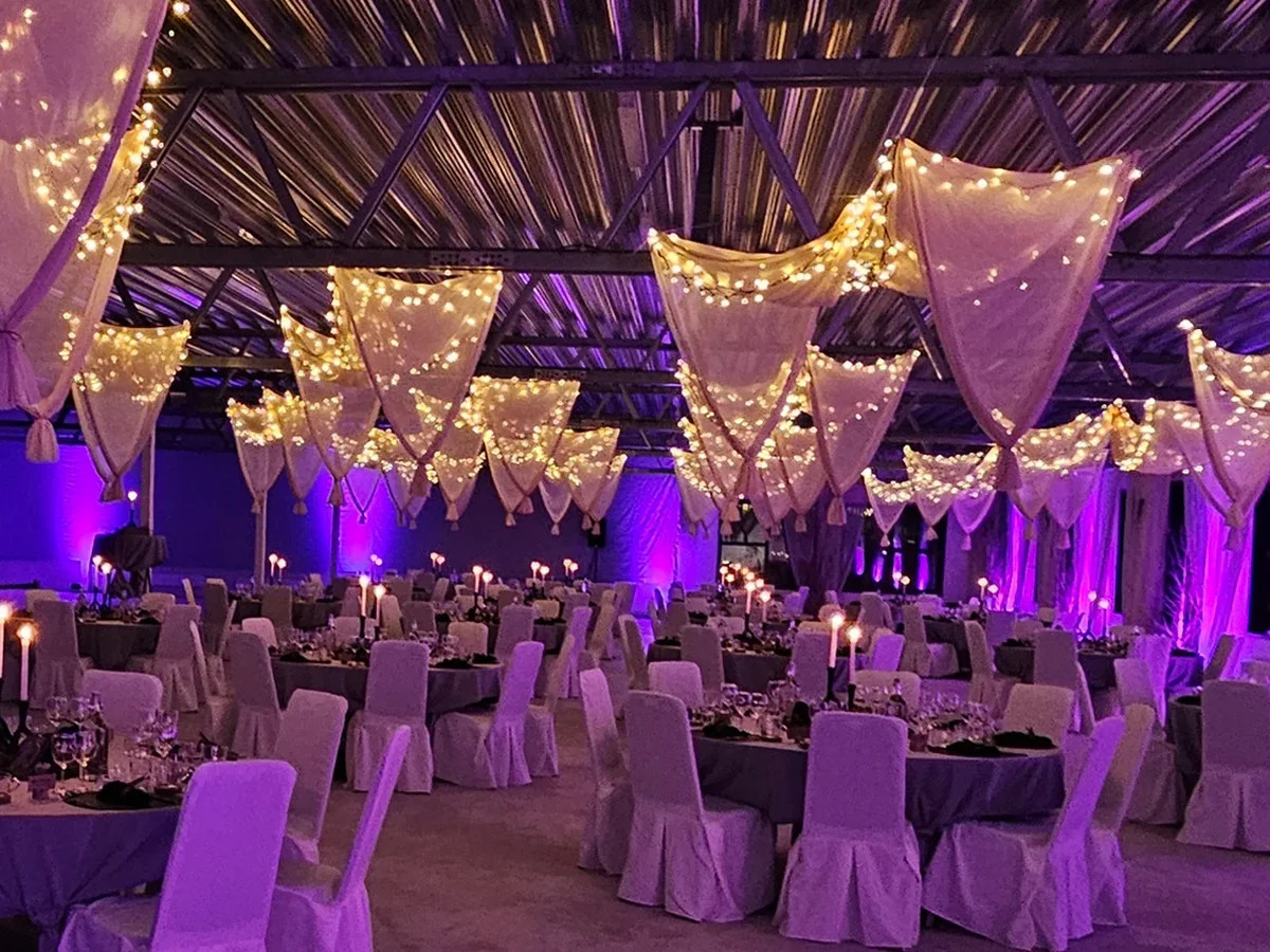 Bröllopslokal med lila uplights, drapering och dukade bord